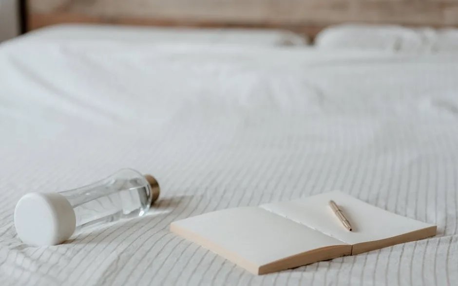 Carnet ouvert et stylo posés sur un lit, pour noter ses heures de sommeil
